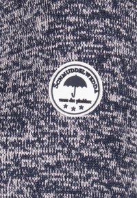 Stickad tröja i marinblå och grå nyanser med ett strukturerat mönster. Har en rund svartvit märkning med en paraply och stjärnor.