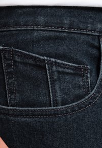 Dark blue denim jeans with a visible back pocket, featuring contrast-stitching and a soft, textured finish. The pocket has a rectangular shape.