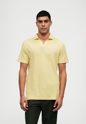 Polo amarillo de manga corta con un diseño de escote en V. Tela texturizada, silueta ajustada, combinado con pantalones verde oscuro.