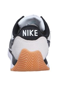 Zapatilla Nike en blanco y negro con un talón de ante texturizado, suela de goma con un patrón de zigzag y un cuello acolchado para mayor soporte.