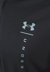 Černé sportovní legíny z texturované tkaniny, s lehce modrým logem na boku. Žebrovaný design přidává vizuální detail.