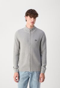 Cardigan grigio con zip, dalla texture a coste, colletto alto e maniche lunghe. Presenta una piccola patch con logo sul petto e polsini aderenti.