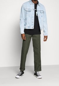 Ljusblå denimjacka, svart t-shirt med tryck, gröna byxor och svarta högstertofflor. Avslappnad, boxig passform; två framfickor på jackan.