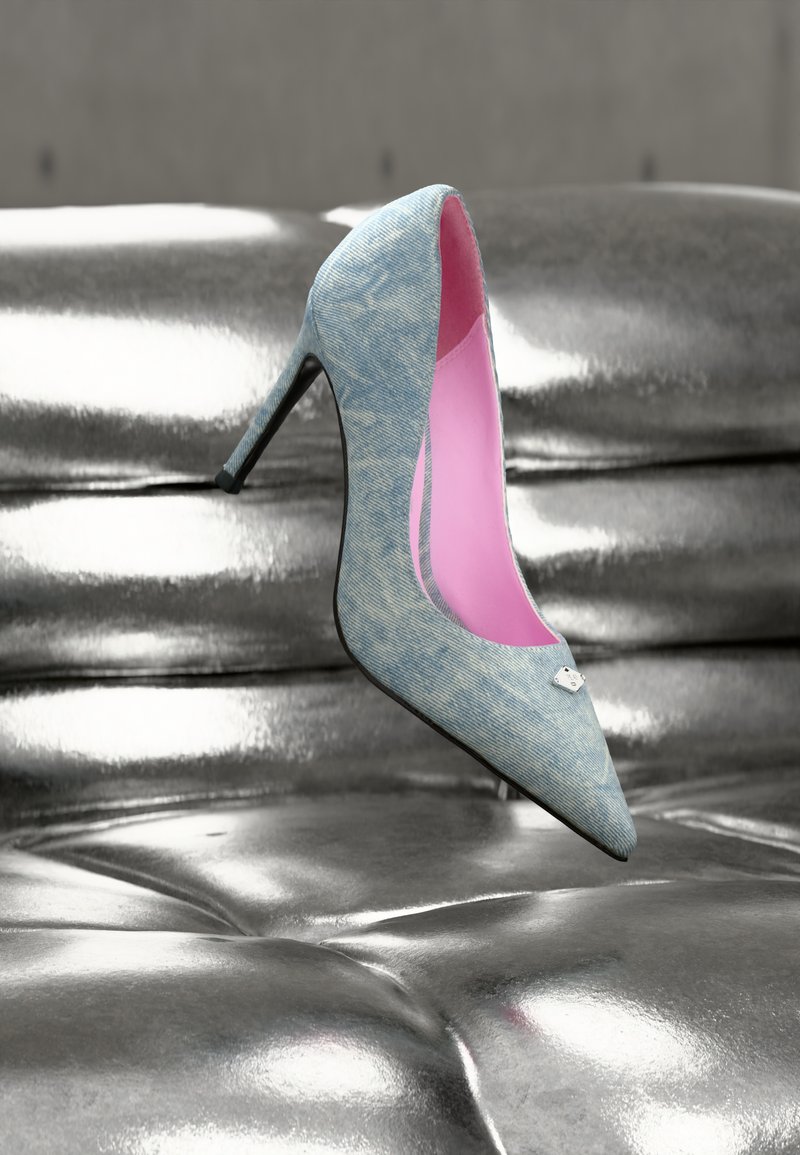 Γόβα με μυτερή μύτη και τακούνι σε υφή που μοιάζει με τζιν, με ροζ εσωτερικό και ασημί μεταλλικές λεπτομέρειες, τοποθετημένη σε μια γυαλιστερή ασημί επιφάνεια.