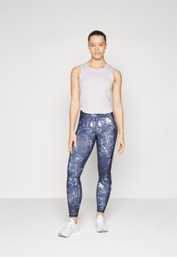 Svetlo šedý crop top s širokými ramienkami; priliehavé námornícke legíny so mramorovým vzorom; biele športové topánky.