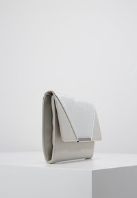 Šedá koženková kabelka na večer s třpytivým stříbrným klopou. Obsahuje jednoduchý, strukturovaný design a malý stříbrný detail pro uzavření.