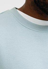 Hanorac albastru deschis cu guler rotund și margine striată. Textură moale, design minimalist, având un guler interior alb contrastant.