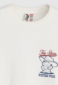 Bílý bavlněný tričko s barevným potiskem kreslené postavy v kovbojském klobouku a textem "Toy Story WESTERN WEAR" níže.