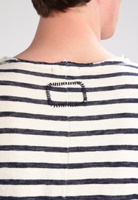 Paskowana bluzka w granatowo-kremowe poziome pasy, okrągły dekolt i haftowany prostokątny detal z tyłu.