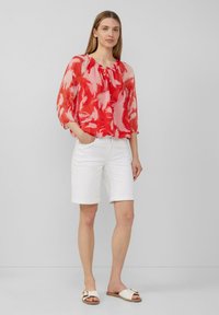 Blouse légère à motifs rouges et roses avec des manches 3/4, associée à un short en denim blanc et des sandales blanches à glissière. Tenue simple et décontractée.