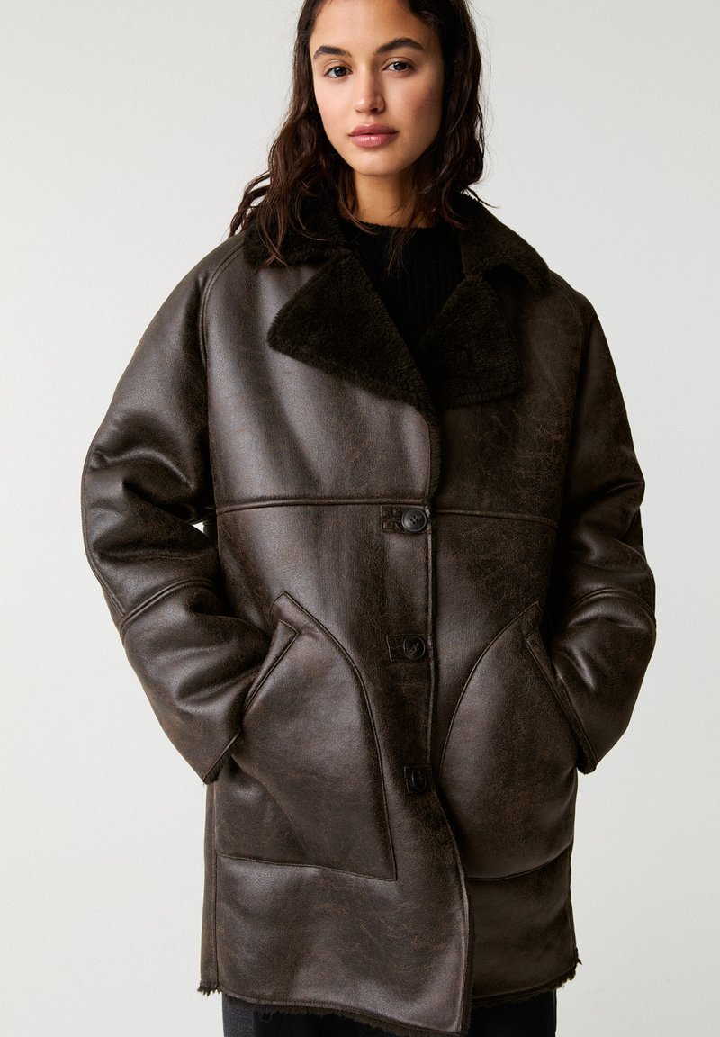 Braune Lederjacke mit einem weichen Fellkragen, großen Fronttaschen und einem Knopfverschluss, strukturierte Oberfläche und lässiger Schnitt.