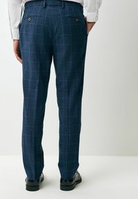 Marineblaue Karohosen mit einer glatten Textur, die blaue Karolinien, Gesäßtaschen und goldene Hardware-Akzente aufweisen. Entworfen mit einer taillierten Passform.