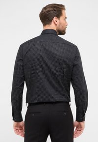 Schwarzes Hemd mit Knopfleiste und weißen Punkten, langen Ärmeln und einem spitzen Kragen. Die Rückseite hat eine glatte Textur und eine taillierte Passform.