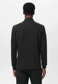 Crna dugorukava polo majica viđena sa stražnje strane. Ima ravni ovratnik, rebraste manžete i glatku teksturu. Jednostavan, klasičan dizajn.