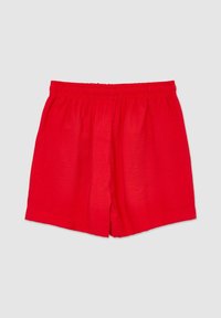 Short ample à taille élastique rouge posé à plat sur un fond gris clair.