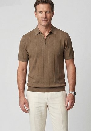 Man met een bruin poloshirt met korte mouwen en lichtbeige broek, staand tegen een effen lichtgrijze achtergrond.