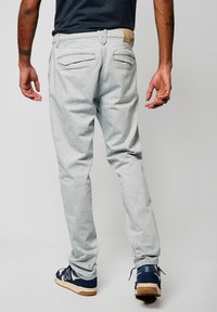 Pantalones gris claro con acabado texturizado, que cuentan con bolsillos traseros y un cinturón tejido en color beige. Combinados con zapatillas azules y una camiseta negra.