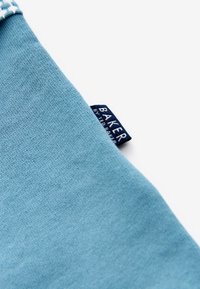 Jasnoniebieska bawełniana tkanina o gładkiej strukturze; posiada ciemnoniebieską tkana metkę z napisem "BAKER" w białych literach.