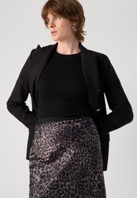 Svart blazer over en svart topp, kombinert med et silkemykt grått leopardmønstret skjørt. Skjørtet har en subtil glans og solid svart midje.