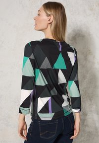 Schwarzes Langarmoberteil mit geometrischem Muster in Grün, Weiß und Lila. Rundhalsausschnitt und strukturierte dreieckige Akzente.