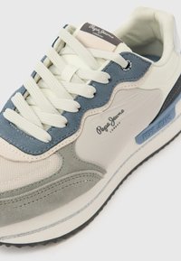 Ελαφρύ αθλητικό παπούτσι με συνδυασμό από υλικά σε κρεμ, μπλε και γκρι χρώματα. Διαθέτει υφή υφάσματος, γυαλιστερές δερμάτινες λεπτομέρειες και έντονη σήμανση.