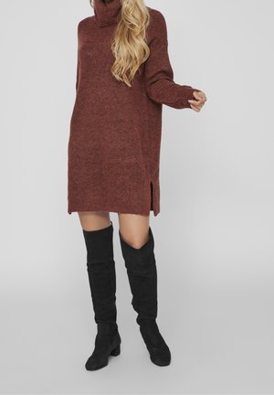 Robe tricotée bordeaux avec col roulé, fentes latérales et manches longues, associée à des bottes en daim noires jusqu'aux genoux.