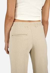 Beige, texturált nadrág gumis derekú és hátsó zsebbel. Az anyag waffle mintázatú, ami extra részletességet és kényelmet biztosít.