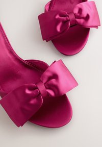 Fuchsia satijnen sandalen met hoge hak en een grote strik op de band, een gladde textuur en een afgeronde open teen ontwerp.