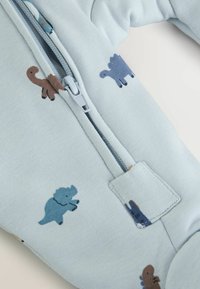 Hellblaues Stoff-Overall mit Reißverschluss, der verschiedene Dinosauriermuster in Braun, Blau und Dunkelblau aufweist. Glatte Textur mit einem Reißverschluss vorne.