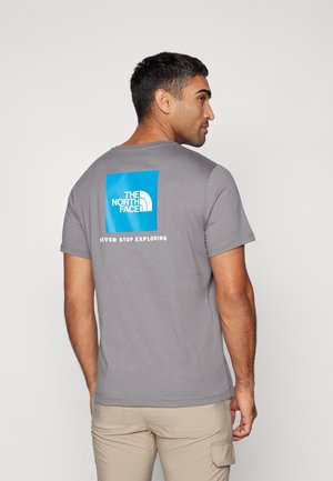 Siva pamučna majica s plavim kvadratnim logotipom s natpisom "THE NORTH FACE" i "NEVER STOP EXPLORING" na leđima. Kratki rukavi, okrugli izrez.