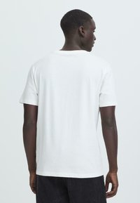 Witte katoenen T-shirt met een ronde hals, korte mouwen en een ontspannen pasvorm, vanuit de achterkant weergegeven. Zachte textuur, eenvoudig ontwerp, geen graphics.