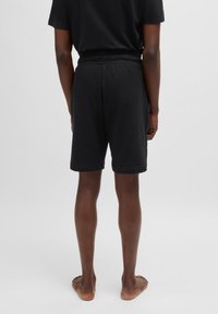 Mustat puuvillahousut, joissa on elastinen vyötärö, sileä pinta ja rento istuvuus. Malli seisoo paljain jaloin ja näyttää luonnollisen ihonsävyn.