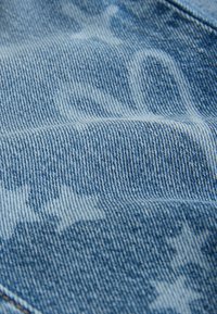 Denimtyg i ljusblått med ett subtilt stjärnmönster. Texturen är slät med en tydlig väv och kontrasterande sömmar.