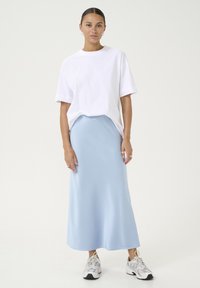 Hvid bomulds-T-shirt med korte ærmer, parret med en lys blå satin midi-nederdel. Modellen har hvide sneakers på. En simpel, afslappet påklædning.