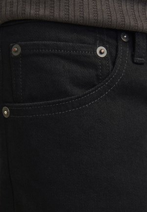 Sorte denimjeans med slim fit og en glat tekstur. Har sølv hardware, nitter og kontrastsyninger nær lommerne.