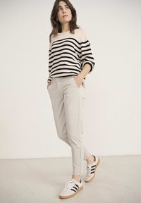 Un pull rayé crème et noir, un pantalon tapered gris clair et des baskets blanches avec des rayures noires et des semelles en gomme. Une tenue simple et moderne.