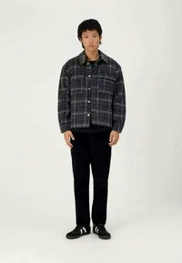 Gray and black plaid button-up shirt with chest pockets, worn over a black T-shirt, paired with black pants and sneakers. Simple design.