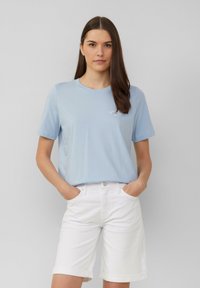Lichtblauwe katoenen T-shirt met een ronde hals en korte mouwen, voorzien van een klein geborduurd detail. Gecombineerd met witte denim shorts.