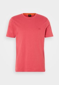T-shirt à manches courtes de couleur corail avec un logo carré en relief subtil sur le côté gauche de la poitrine et une étiquette noire à l'intérieur du col.