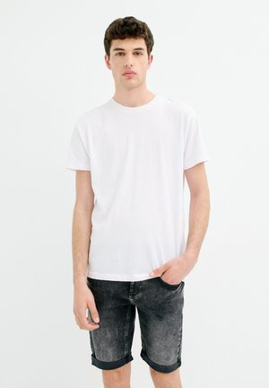 Camiseta de algodón blanca con cuello redondo, combinada con pantalones cortos de mezclilla gris. Los pantalones cortos presentan un diseño desgastado y puños enrollados.