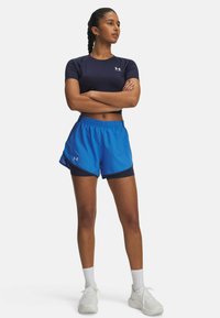 Haut de sport à manches courtes de couleur marine associé à un short bleu avec une taille élastique et des accents en maille sur les côtés. Des baskets blanches parachèvent le look.
