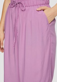 Pantalons violet clair avec taille élastique, cordon de serrage et poches latérales, fabriqués dans un tissu lisse et léger.
