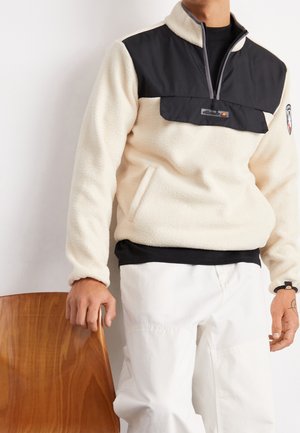 Pullover in pile color crema con un pannello frontale zip nero. Caratterizzato da un colletto alto, tasche laterali e dettaglio del logo sul petto.