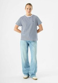 Marineblauwe en witte gestreepte katoenen t-shirt met een ronde hals, gecombineerd met lichtblauwe wijde spijkerbroeken en witte sneakers.