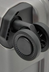 Schwarzes Radmechanismus, der an einem strukturierten silbernen Koffer befestigt ist. Das Rad hat eine flache, runde Oberfläche mit geriffelten Akzenten für besseren Halt.