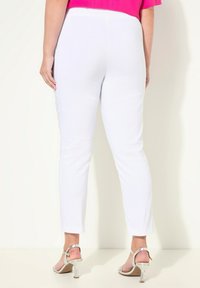Pantalons blancs ajustés avec une texture lisse et longueur cheville, associés à des talons aiguilles argentés à lanières. Le design comprend des détails latéraux élégants.
