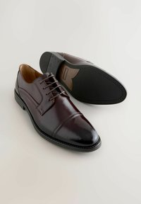 Zapatos de vestir de cuero marrón con acabado pulido, forma estrecha y alargada, punta redonda y diseño con cordones; suela de goma con detalle de costura.