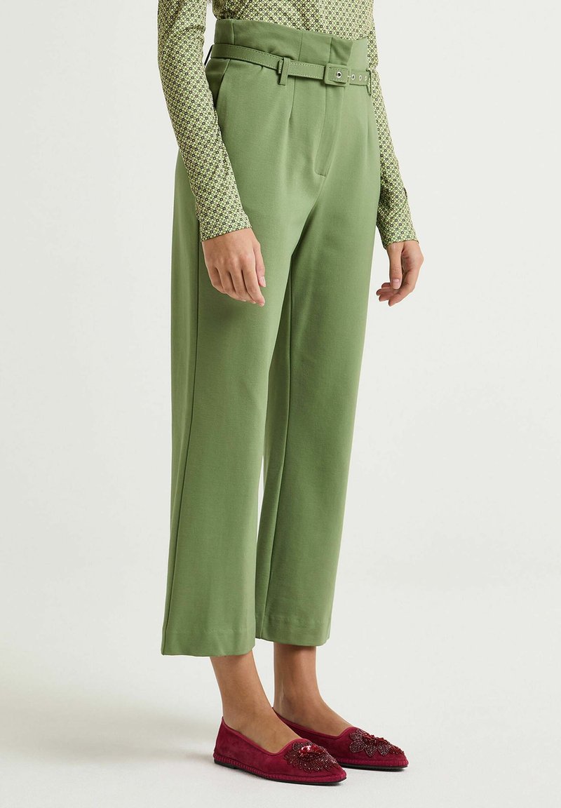 Green wide-leg trousers with a belt, featuring a smooth texture and tailored fit. Styled with burgundy embellished slip-on flats.