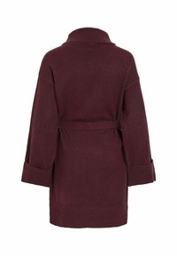 Robe tricotée bordeaux avec un col châle, coupe oversize, taille ceinturée et poignets repliés. Texture douce avec un motif uni.