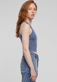 Svetlo modra nareznica s širokimi trakovi, v kombinaciji z svetlo modrimi jeans hlačami z visokim pasom. Gladek material in prilegajoča zasnova.